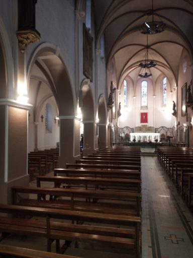 Intérieur d'une église avec des bancs en bois et un chœur lumineux à l'arrière.